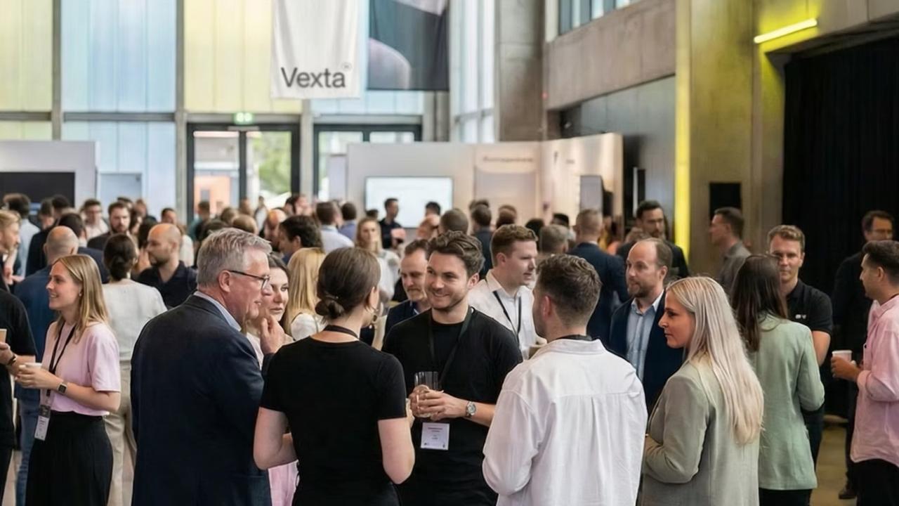 Crowd at a networking reception in a bright modern atrium, people talking with drinks