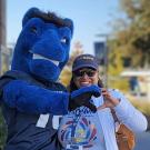 Person in sunglasses and cap smiling with a blue mascot outdoors