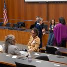 Meeting room with wooden dais and U.S. flag; attendees at desks, small group conversing